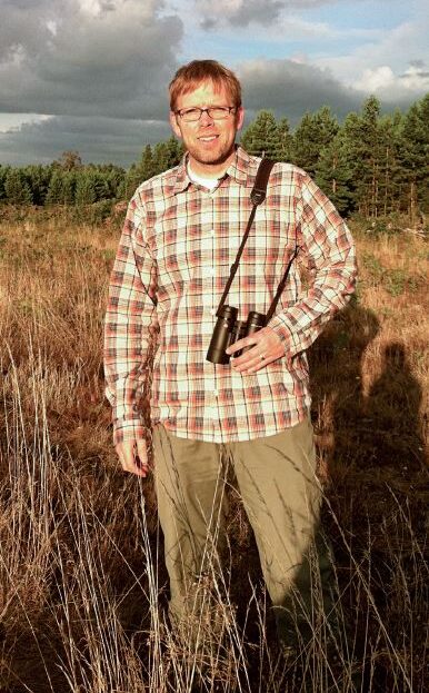 Man stands in field with binoculars.