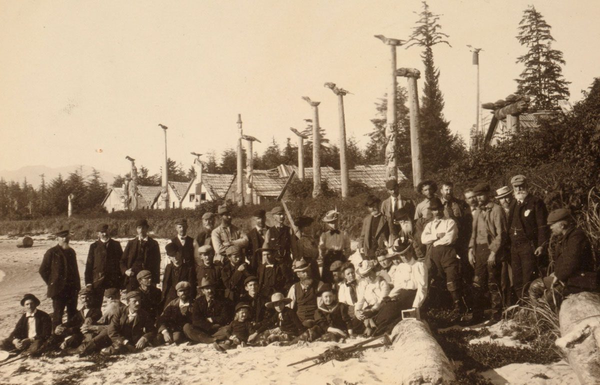 The Harriman Expedition members posed on the beach at Cape Fox Village, Alaska, 1899. Here they found an abandoned Tlingit village with totem poles still standing. Image from Wikimedia Commons.