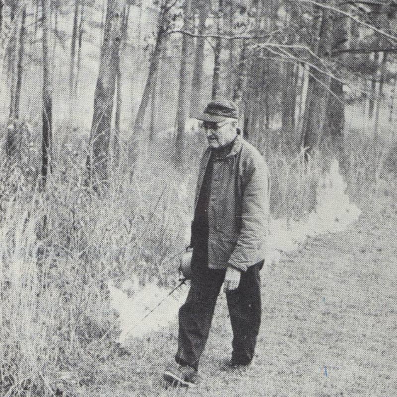 Black and white photo of a person using a drip torch to start a prescribed fire.