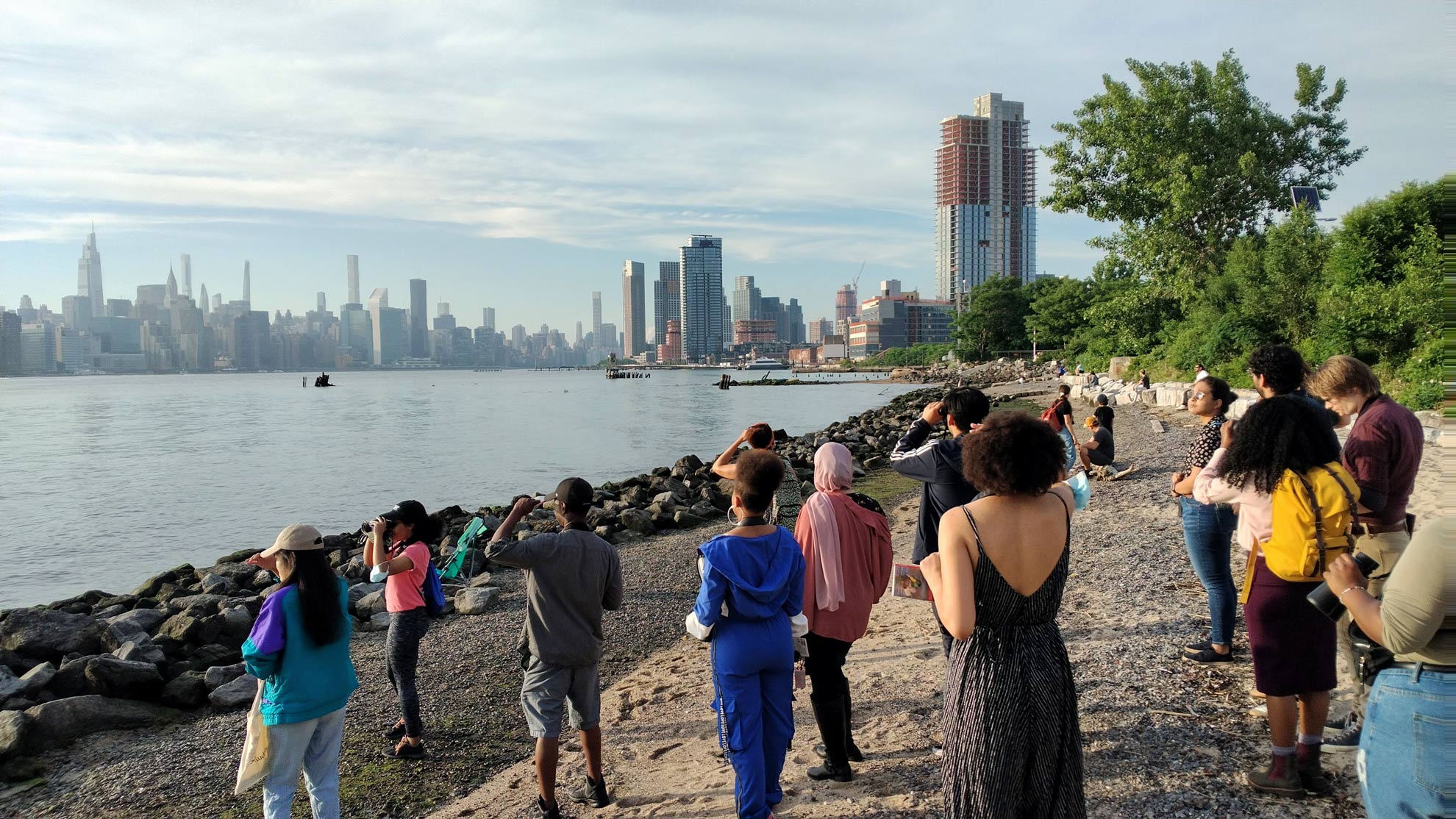 a group of men and women watch birds with a view of the New York skyline in the distance