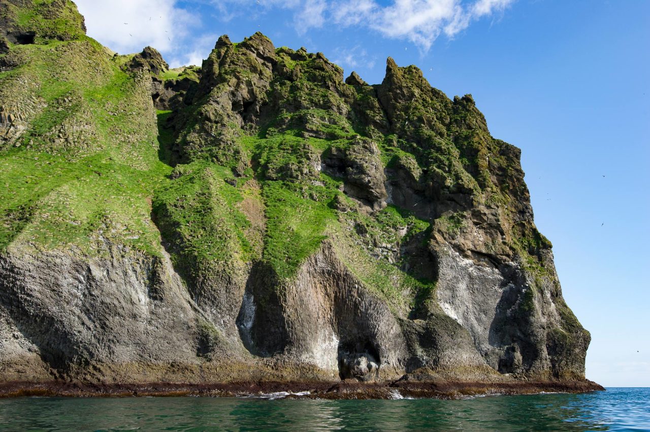 A tall, jagged, very steep island partially covered with grass 