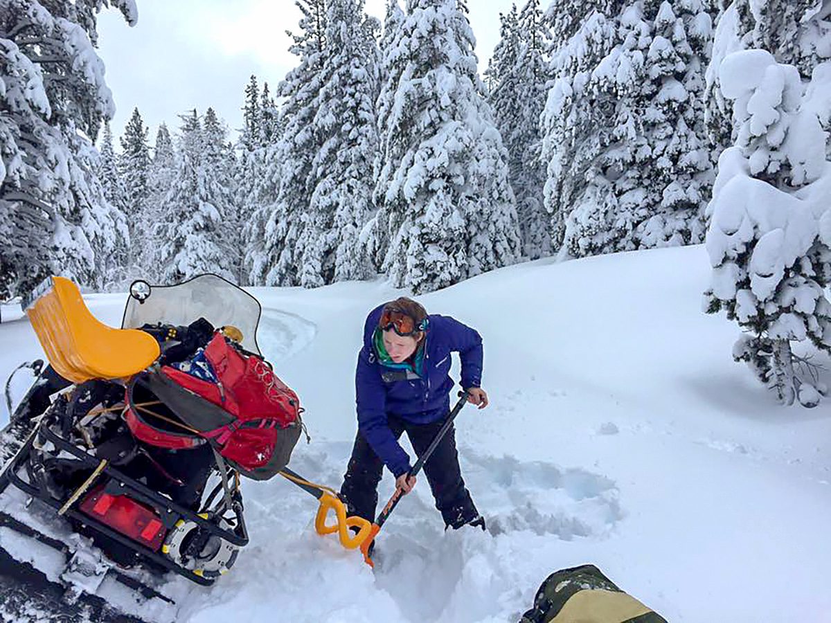 a researcher digs her snowmobile out of a deep drift of snow