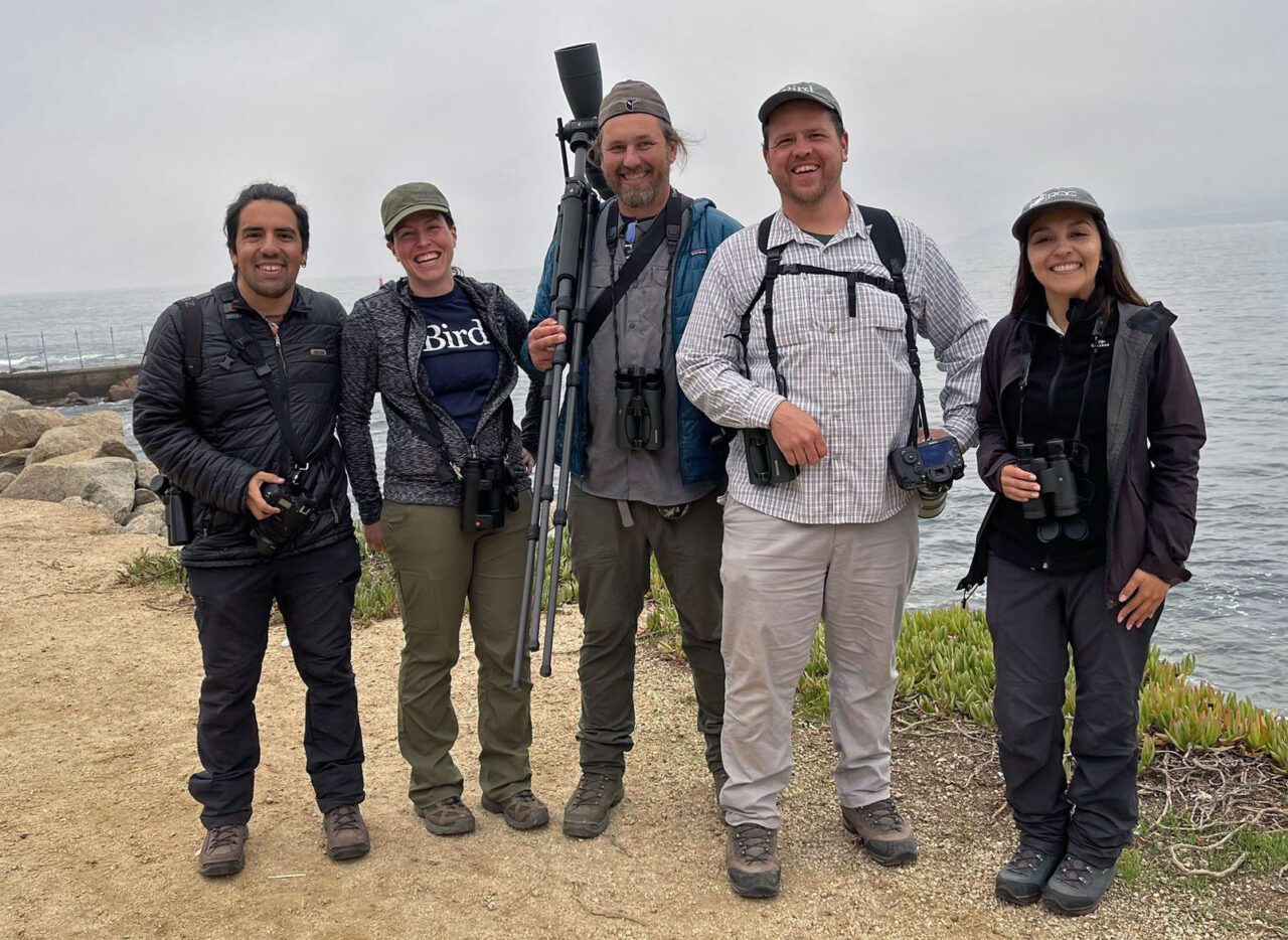 Four people stand with ocean behind.