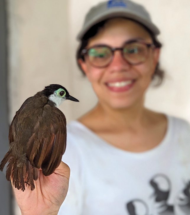 Woman with glasses and cap holds a brown bird with a white face.