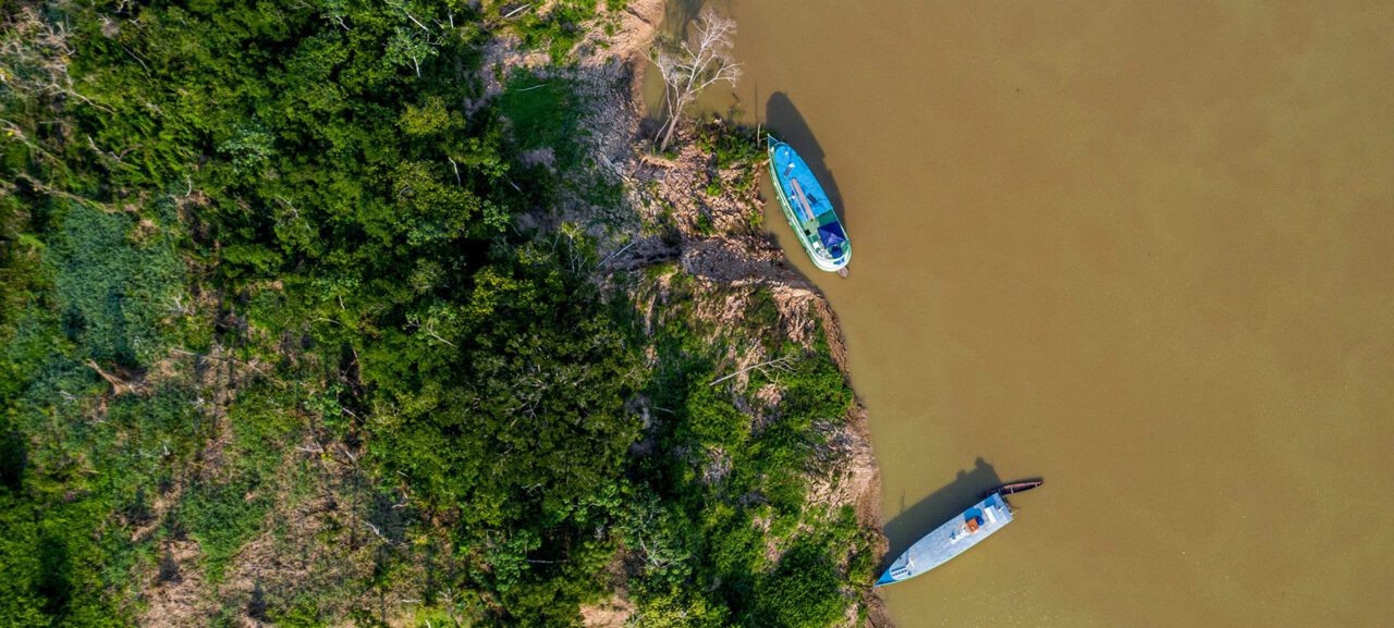 Aerial view of two blue boats on a greenish river next to forest.