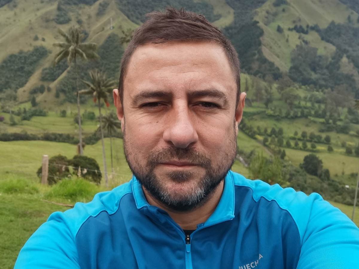 Man in blue shirt with tropical mountains in background.