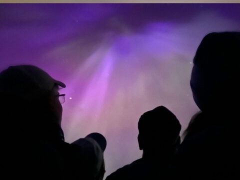 Silhouette of people against purple sky of Aurora Borealis.